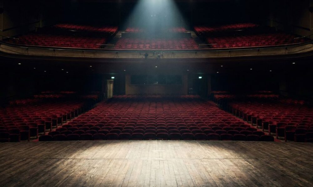 A single spotlight on an empty theater stage.
Featured Image Description: A cinematic, high-contrast photo of an empty luxury auditorium with a single spotlight illuminating a vacant wooden stage.
Featured Image Title: The Empty Stage of Business
