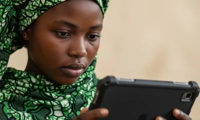 A young Nigerian woman in a green headscarf focused on a digital tablet, illustrating the hardware requirements for Secure Electronic Voting in Nigeria.