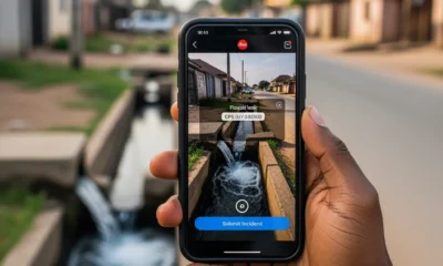 A close-up of a person using mobile apps for public infrastructure reporting to document a burst water pipe on a Nigerian street, illustrating the prevention of financial and water loss.