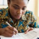 A focused Nigerian female investigator examining a staff payroll ledger to identify ghost workers in the primary school.