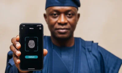 A middle-aged Nigerian man in a navy blue agbada showcasing a secure mobile identity interface, representing Digital IDs Future National Security.
