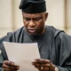 A middle-aged Nigerian man in traditional agbada intensely reviewing a legal document, demonstrating the importance of avoiding pit snare of law.
