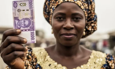 A close-up of a Nigerian market trader holding a 1000 Naira note, representing the Physical Cash King in West African commerce.