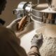 Farmer's hands inspecting white cassava flour next to a raw tuber and processing machinery.
