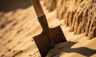 A worn wooden shovel partially buried under a heavy mound, loose sand.