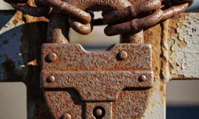 A close-up rusted padlock and cha a closed metal gate.