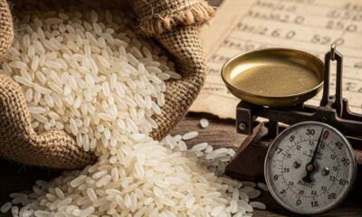 Close-up rice sack, a scale, coins, and a worn price list on wood.