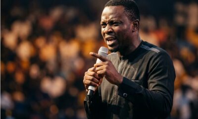 Nigerian comedian performing on stage at indoor arena with crowd visible in background and stage lights creating dramatic effectFeatured Image Description:
Digital photograph of a Nigerian comedian performing at a major comedy show in Lagos. The comedian stands center stage holding a wireless microphone, mouth open mid-performance. Stage lighting creates dramatic shadows. Audience visible in foreground as dark silhouettes with occasional phone screens glowing. Arena setting suggests capacity over 3,000 attendees. Professional production values visible in lighting rig and sound equipment. Date indicates 2026 performance.Featured Image Title:
nigerian-comedian-live-performance-arena-2026.jpg