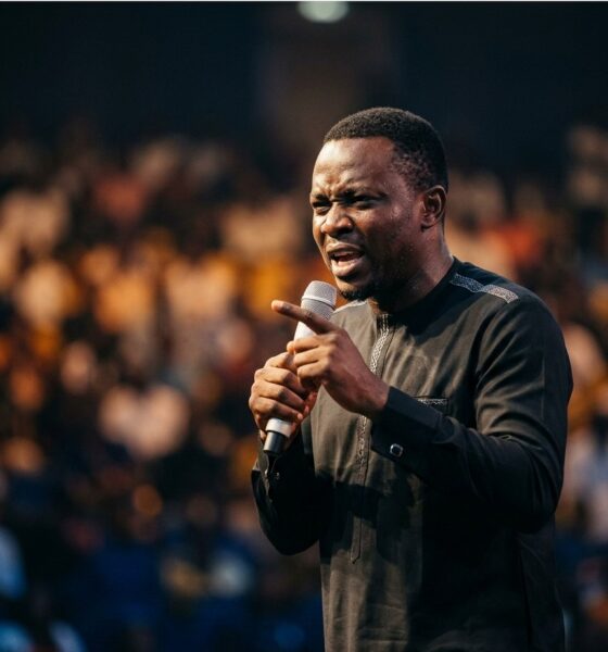 Nigerian comedian performing on stage at indoor arena with crowd visible in background and stage lights creating dramatic effectFeatured Image Description:
Digital photograph of a Nigerian comedian performing at a major comedy show in Lagos. The comedian stands center stage holding a wireless microphone, mouth open mid-performance. Stage lighting creates dramatic shadows. Audience visible in foreground as dark silhouettes with occasional phone screens glowing. Arena setting suggests capacity over 3,000 attendees. Professional production values visible in lighting rig and sound equipment. Date indicates 2026 performance.Featured Image Title:
nigerian-comedian-live-performance-arena-2026.jpg