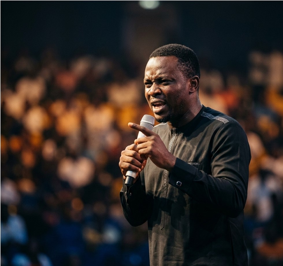 Nigerian comedian performing on stage at indoor arena with crowd visible in background and stage lights creating dramatic effectFeatured Image Description:
Digital photograph of a Nigerian comedian performing at a major comedy show in Lagos. The comedian stands center stage holding a wireless microphone, mouth open mid-performance. Stage lighting creates dramatic shadows. Audience visible in foreground as dark silhouettes with occasional phone screens glowing. Arena setting suggests capacity over 3,000 attendees. Professional production values visible in lighting rig and sound equipment. Date indicates 2026 performance.Featured Image Title:
nigerian-comedian-live-performance-arena-2026.jpg