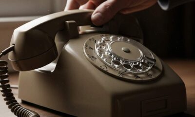 A hand placing a vintage telephone receiver down on a wooden surface.