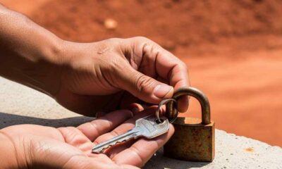 Hands holding a new key against a rusted padlock on a concrete ledge.