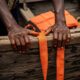 Close-up of weathered hands gripping the splintered wooden edge of a boat, with a life jacket str...