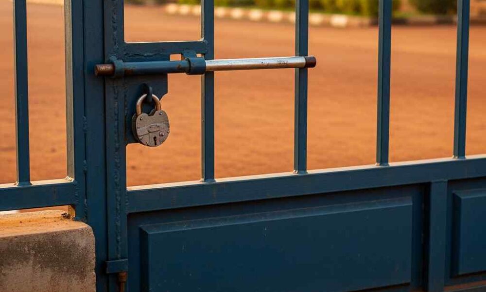 A closed steel security gate at a Nigerian school entrance during morning light.