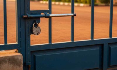 A closed steel security gate at a Nigerian school entrance during morning light.