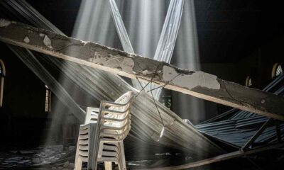 A white plastic chair is flattened under a large concrete beam amidst debris hall