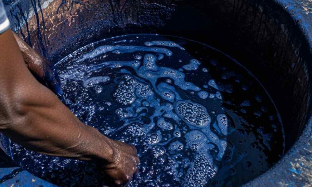 Close-up indigo dye bubbling stone pit with a person's arm stirring the liquid