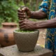 Hands crush leaves in stone mortar.