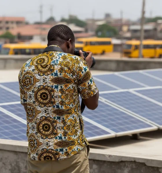 Rooftop scene: Photographer adjusts lens with solar panels and buses afar.