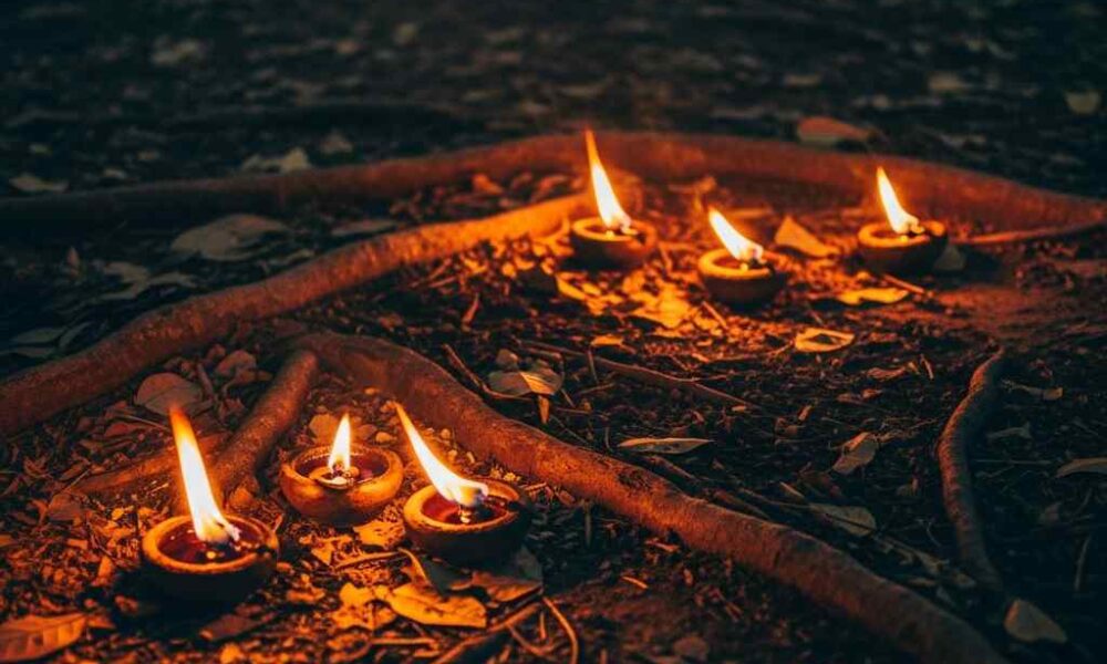 Several small oil lamps flicker on the ground amidst forest roots and leaves