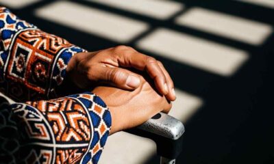 Person's hands gripping a suitcase handle, wearing a patterned shirt.