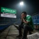 a despondent Nigerian football supporter in a green jersey, sitting alone in a darkened stadium with his head in his hands. In the background, a large digital scoreboard displays "FIFA WORLD CUP 2026 QUALIFICATION COMPLETED: DR CONGO QUALIFIED - NIGERIA MISSES OUT." A newspaper on the concrete floor carries the headline "SUPER EAGLES' DREAM DASHED.