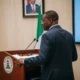 Man at podium in Abuja, coat of arms blurred.