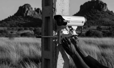A digital security camera mounted on a concrete pole overlooking a rocky rural