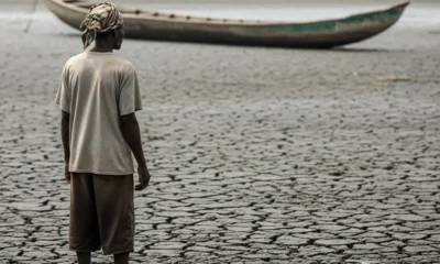 Fisherman stands on cracked mud with canoe in distance.
