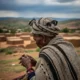 Elderly woman listens on hill, stormy sky behind.