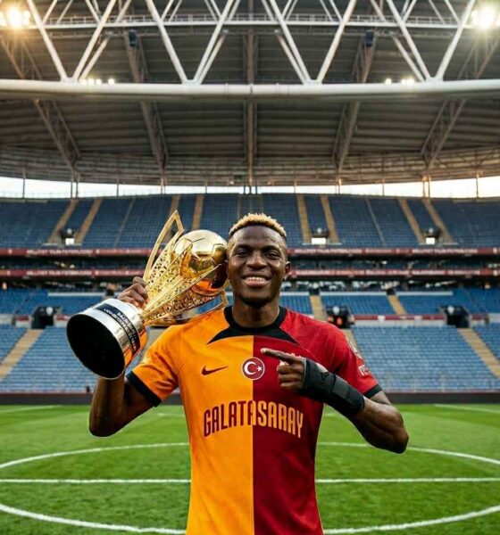 Victor Osimhen in a Galatasaray jersey (yellow and red halves) standing triumphantly on the pitch at RAMS Park in Istanbul. He is raising a large golden football trophy to the crowd. A medical brace is visible on his right forearm. In the background, thousands of blurred fans hold yellow and red flares and "ultrAslan" flags.